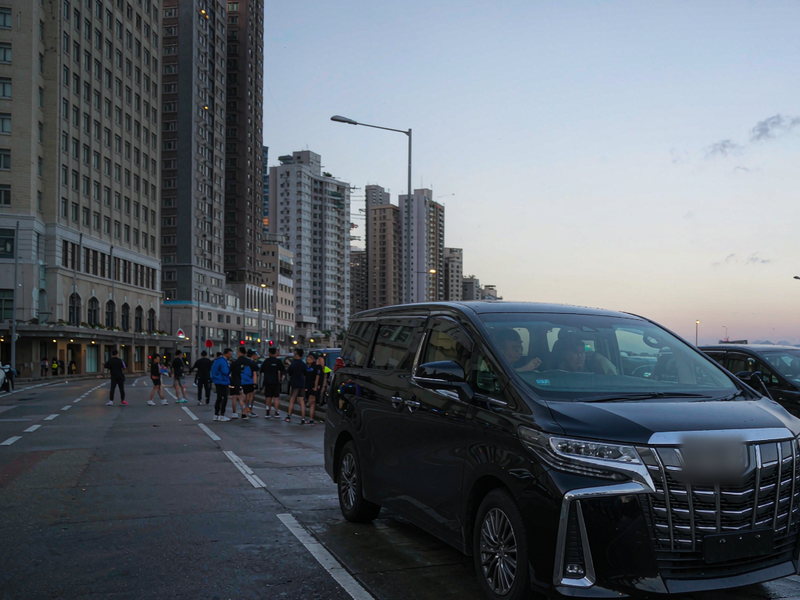渣打香港马拉松2027赛日清晨，尖沙咀街边的黑色七座商务车与热身中的跑者
