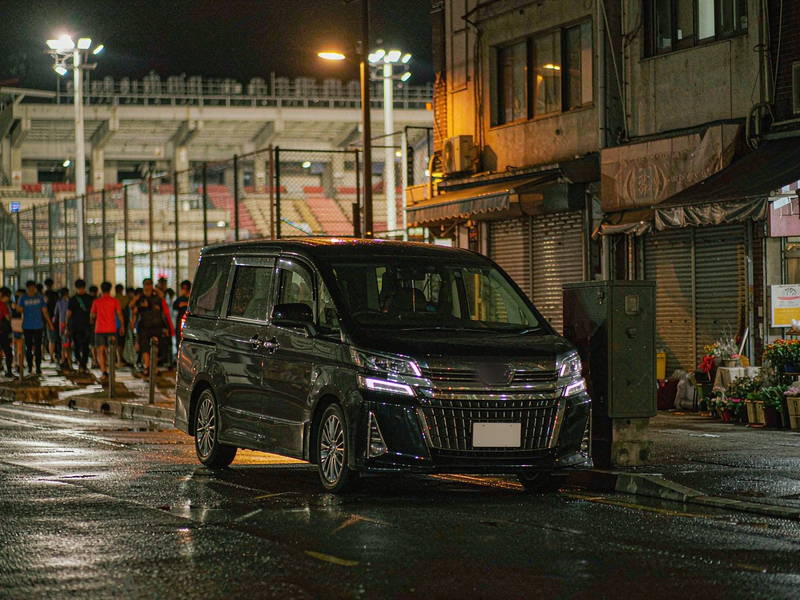 夜间球场外的街道，看台灯光下人群散去，一辆黑色七座豪华商务车在路边等候
